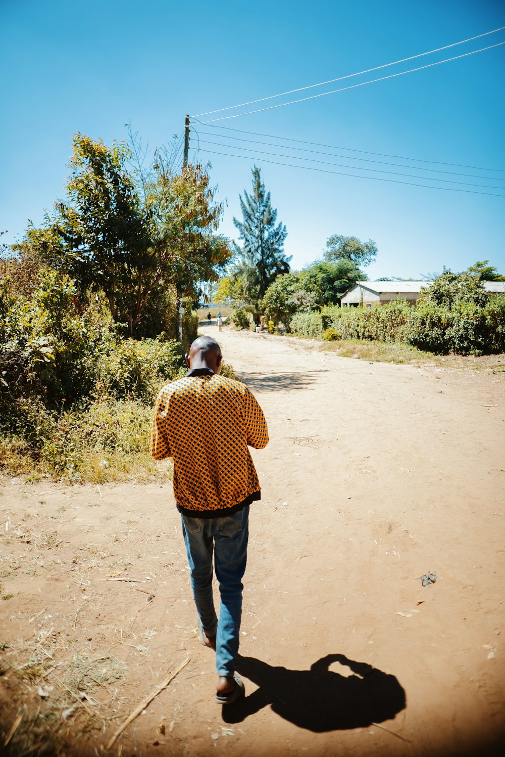 a man walking down a dirt road next to a forest