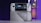 A handheld gaming console with a screen displaying a game library menu is placed on top of its packaging. The console features various buttons, a joystick, and a circular light around the left joystick. The background is blurred with purple, yellow, and blue tones.