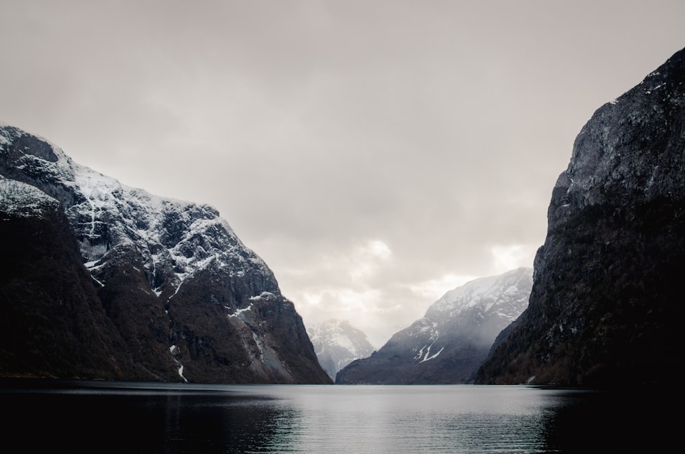 a body of water surrounded by mountains under a cloudy sky