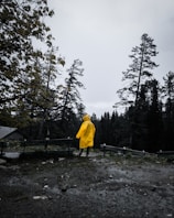 A bright yellow raincoat hanging on a rustic wooden fence with raindrops glistening around it.