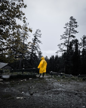 A bright yellow raincoat hanging on a rustic wooden fence with raindrops glistening around it.