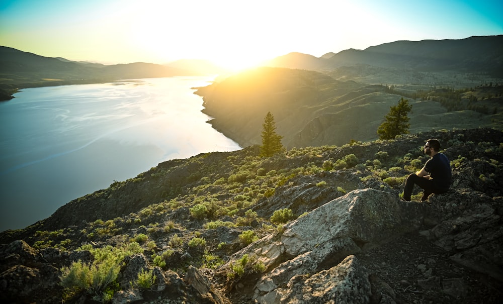 a man sitting on top of a mountain next to a lake