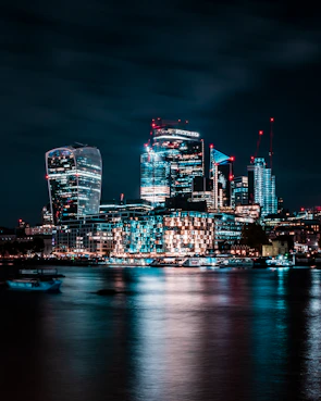 A modern city skyline at night with illuminated skyscrapers reflecting on a calm river.