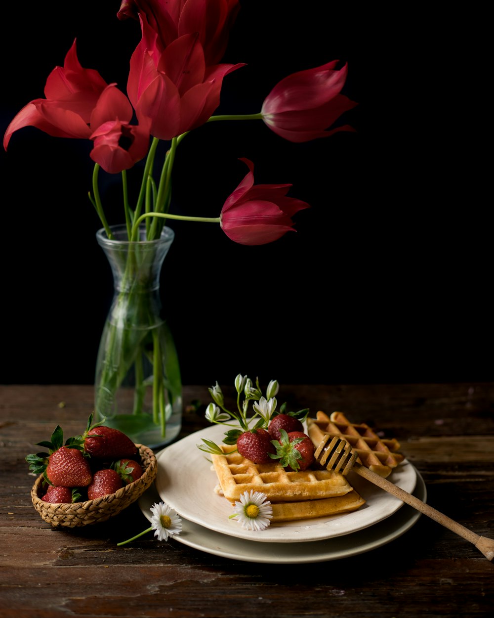 a plate topped with waffles and strawberries next to a vase of flowers