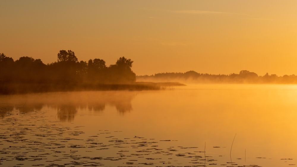 the sun is setting over a calm lake