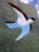 A metal sculpture features a bird-shaped cutout that reveals a clear blue sky with fluffy white clouds. The surface of the sculpture has a textured green appearance, contrasting with the bright sky seen through the cutout.