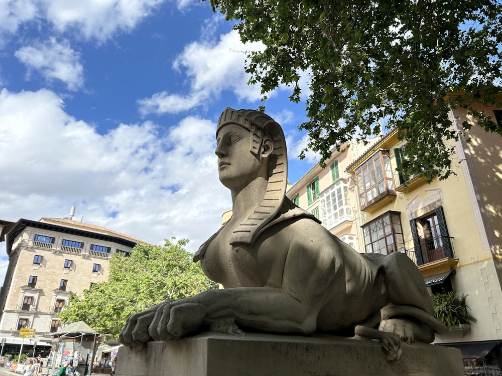 Una estatua de una esfinge en un pedestal frente a un edificio