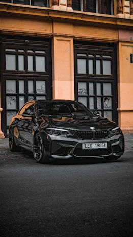A sleek car with a personalized golden license plate parked in front of a modern building.