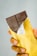 A hand holding a partially unwrapped dark chocolate bar with a gold foil wrapper. The chocolate bar has intricate designs etched on the surface.