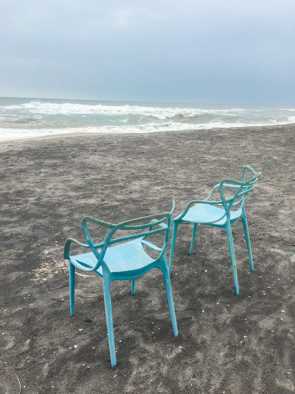 a couple of blue chairs sitting on top of a sandy beach