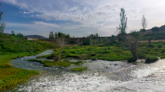 A serene landscape featuring clear water flowing over smooth stones beneath a cloudy sky.