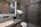 A modern bathroom with geometric patterned tiles on the shower wall, a marble countertop sink, and elegant lighting. Shelves with toiletries and a small plant add a touch of decor, and the overall design features sleek lines and neutral colors.