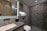 A modern bathroom with geometric patterned tiles on the shower wall, a marble countertop sink, and elegant lighting. Shelves with toiletries and a small plant add a touch of decor, and the overall design features sleek lines and neutral colors.