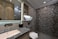 A modern bathroom with geometric patterned tiles on the shower wall, a marble countertop sink, and elegant lighting. Shelves with toiletries and a small plant add a touch of decor, and the overall design features sleek lines and neutral colors.