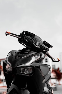 A sleek black motorcycle with an angular design is prominently featured, showcasing sharp headlights and a modern appearance. The background is blurred, highlighting the motorcycle's glossy finish and intricate details.