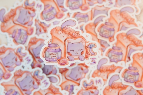 A collection of whimsical stickers featuring a cartoon cat character with closed eyes, resting beside a purple jar labeled 'star jam'. The cat is partially covered with a large piece of toast and surrounded by colorful, dreamy elements.