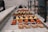An assortment of colorful pastries and desserts are neatly arranged on a marble countertop. The selection includes pieces of cheesecake, orange and yellow square-shaped pastries, and beautifully decorated eclairs. Bright colors contrast with the soft, muted tones of the counter and background.