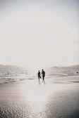 A couple walking hand in hand along a sandy path, the soft sand and warm light creating a cinematic feel.