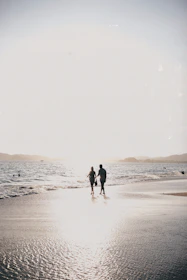 A candid shot of a couple walking hand-in-hand along a sandy beach at sunset, their smiles glowing.