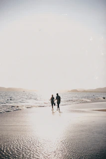 A candid frame of a couple walking hand in hand along a sun-warmed beach at sunset.