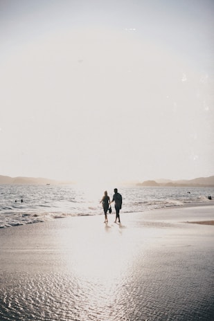 A couple holding hands on a beach at sunset, symbolizing a romantic honeymoon trip.