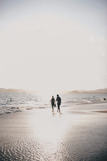 A golden sandy beach at sunset with gentle waves and a couple walking hand in hand.
