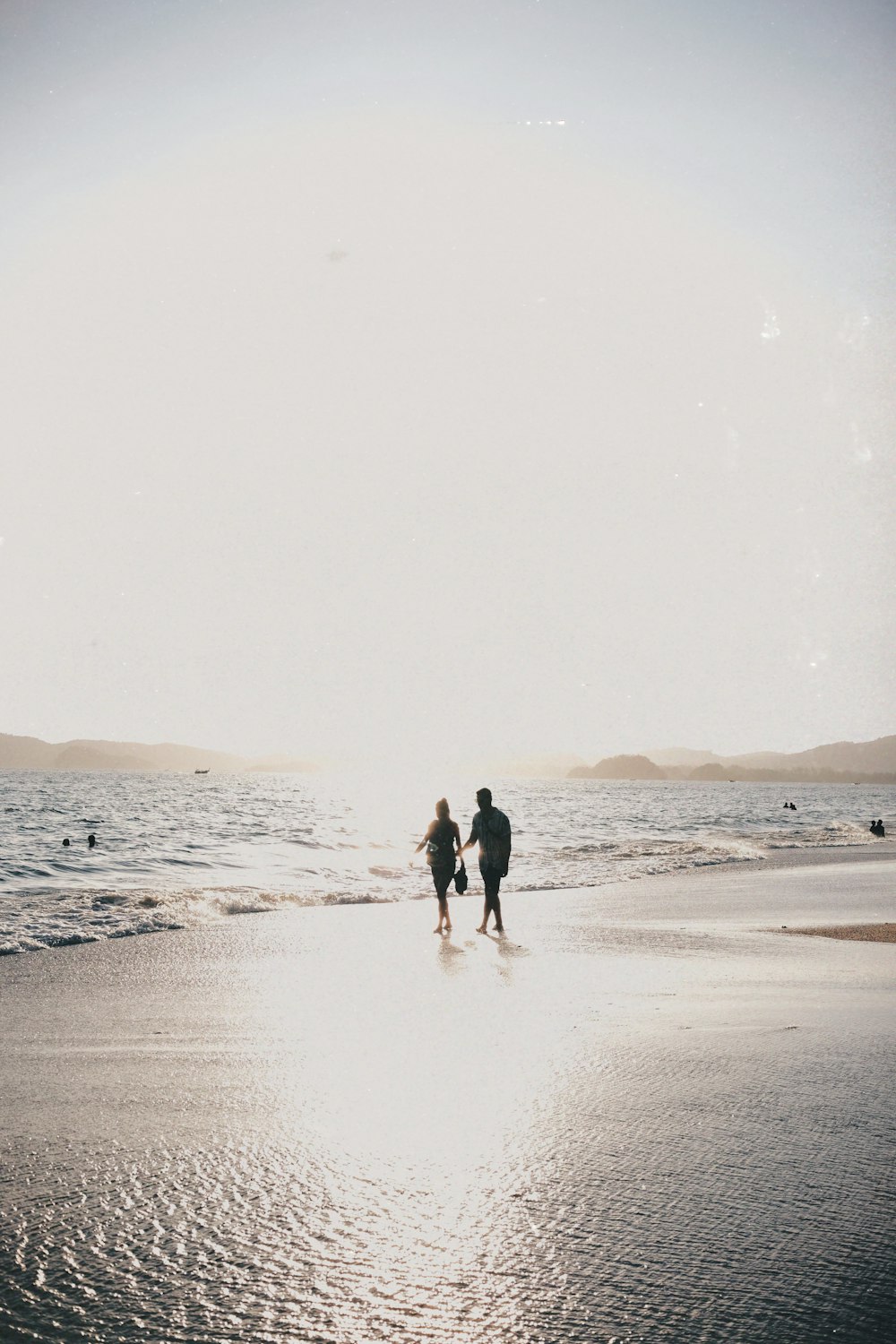 a couple of people walking along a beach next to the ocean