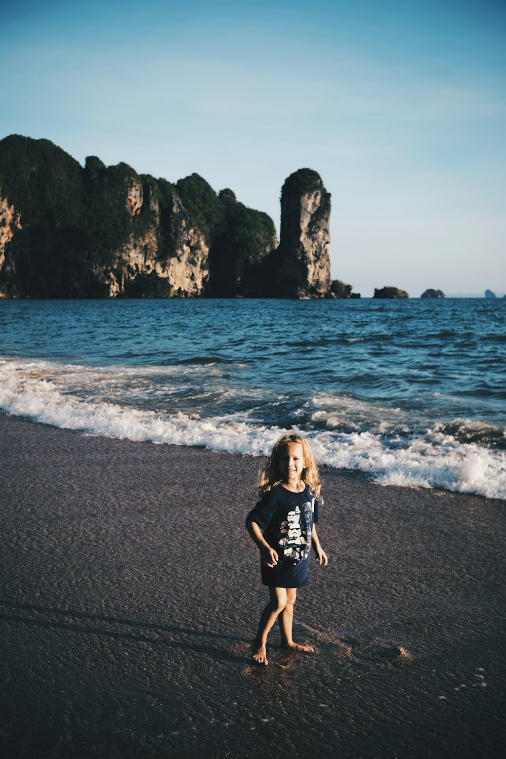 a little girl standing on top of a beach next to the ocean