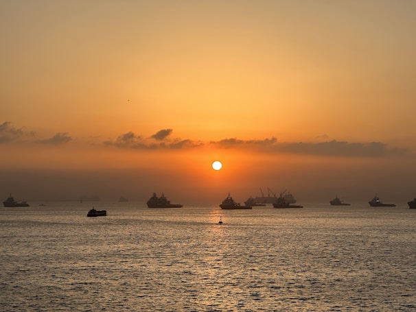 A panoramic view of a fleet of ships sailing on calm ocean waters at sunset.