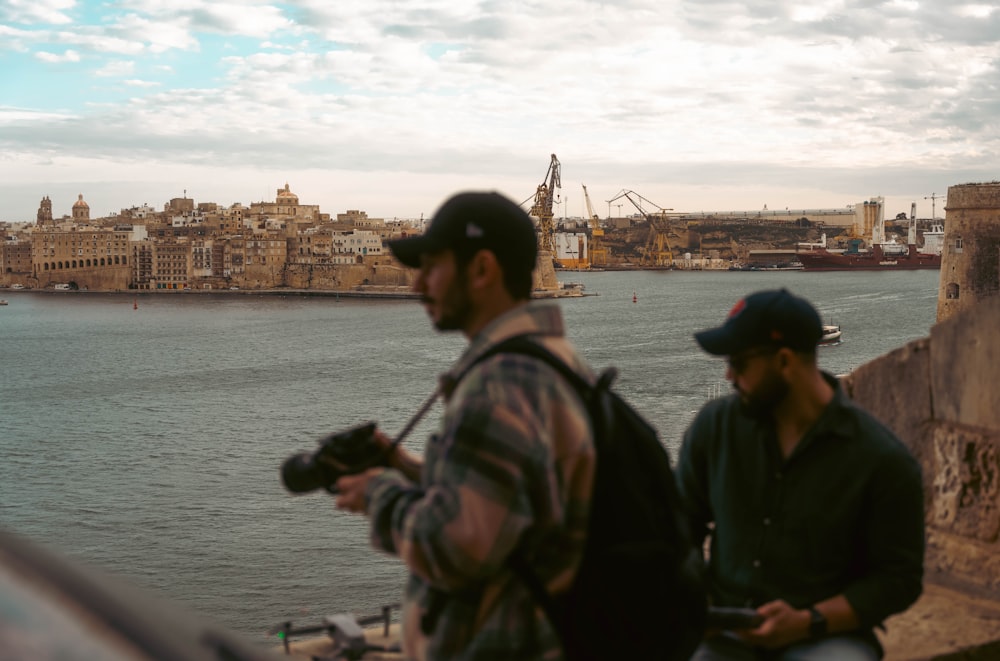 a couple of men standing next to each other near a body of water