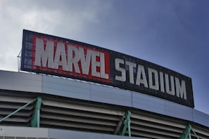 A large sign displaying the words 'Marvel Stadium' is mounted on the upper section of a building. The letters are prominently displayed with 'Marvel' in bold red and 'Stadium' in white. The structure below the sign features a combination of metallic and green elements.