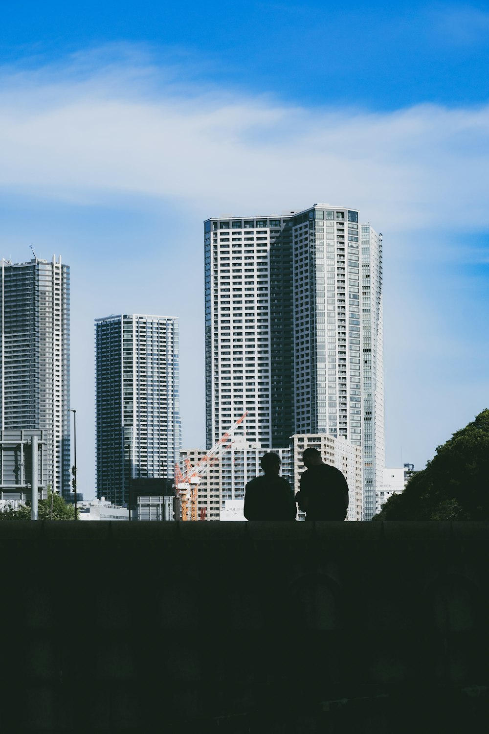 a couple of people sitting on a bench in front of tall buildings