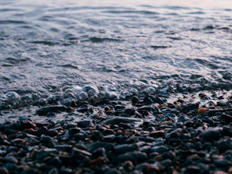Close-up of gentle waves lapping against smooth stones, bathed in warm beige light.