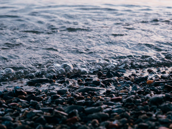 Close-up of gentle waves lapping against smooth stones, bathed in warm beige light.