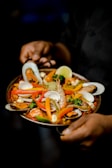 a person holding a plate of food with shrimp and vegetables