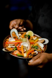 a person holding a plate of food with shrimp and vegetables