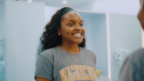 A college girl smiling shyly in a bathroom mirror reflection.