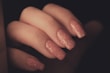 A close-up view of a hand with long, sparkly pink glitter nail polish on the fingernails. The nails are neatly manicured and have a glossy finish, emphasizing the sparkles in the polish.