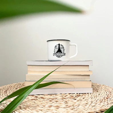 Cozy lifestyle scene featuring a stylish ceramic mug beside a stack of books and a plant.