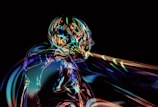 A futuristic, abstract depiction of a humanoid figure rendered in vibrant, iridescent colors against a black background. The form is composed of swirling, liquid-like patterns, creating a dynamic and ethereal effect.