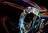 An abstract, futuristic image featuring a human-like figure with an iridescent, reflective surface surrounded by swirling neon lights and colors in a dark environment.
