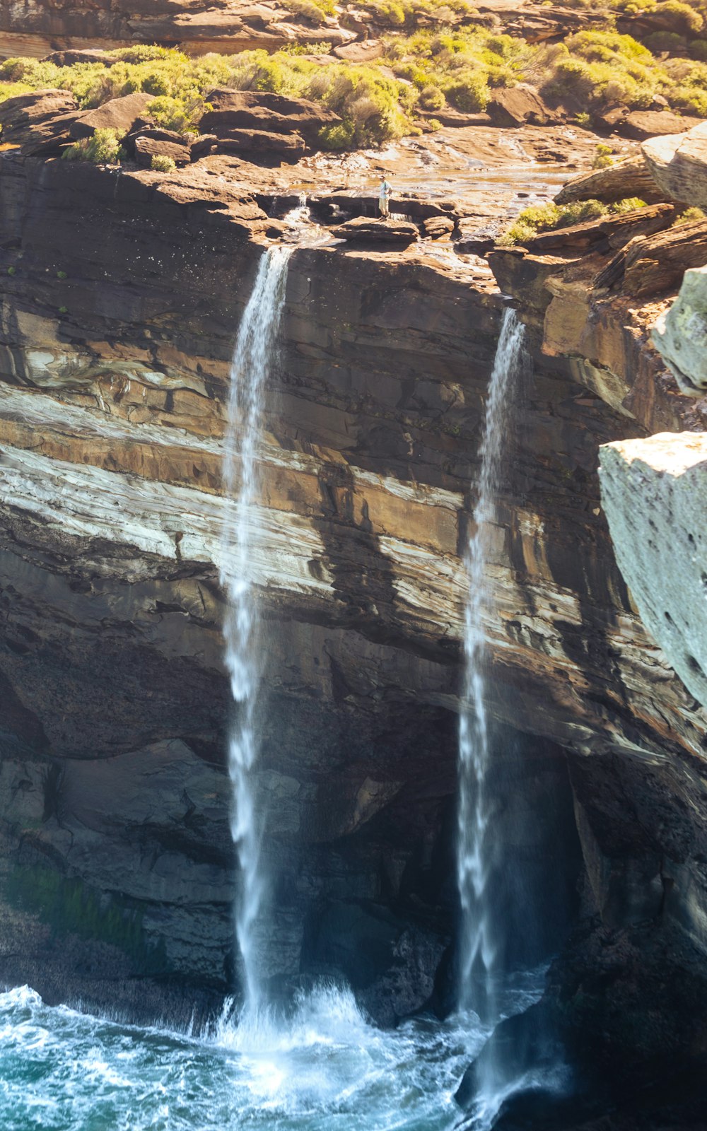 a couple of tall waterfalls sticking out of the side of a cliff