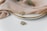 A close-up of elegant jewelry including a gold and silver ring resting on a white plate with a gold rim. Soft beige fabric drapes over the plate, adding a touch of luxury. A small green branch accompanies the setup, enhancing the sophisticated look.