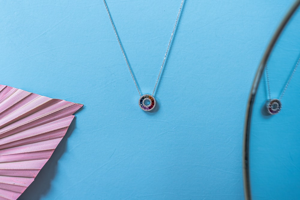 two necklaces on a blue background next to a fan