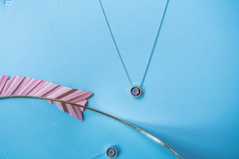 a blue background with a pink flower and a silver necklace