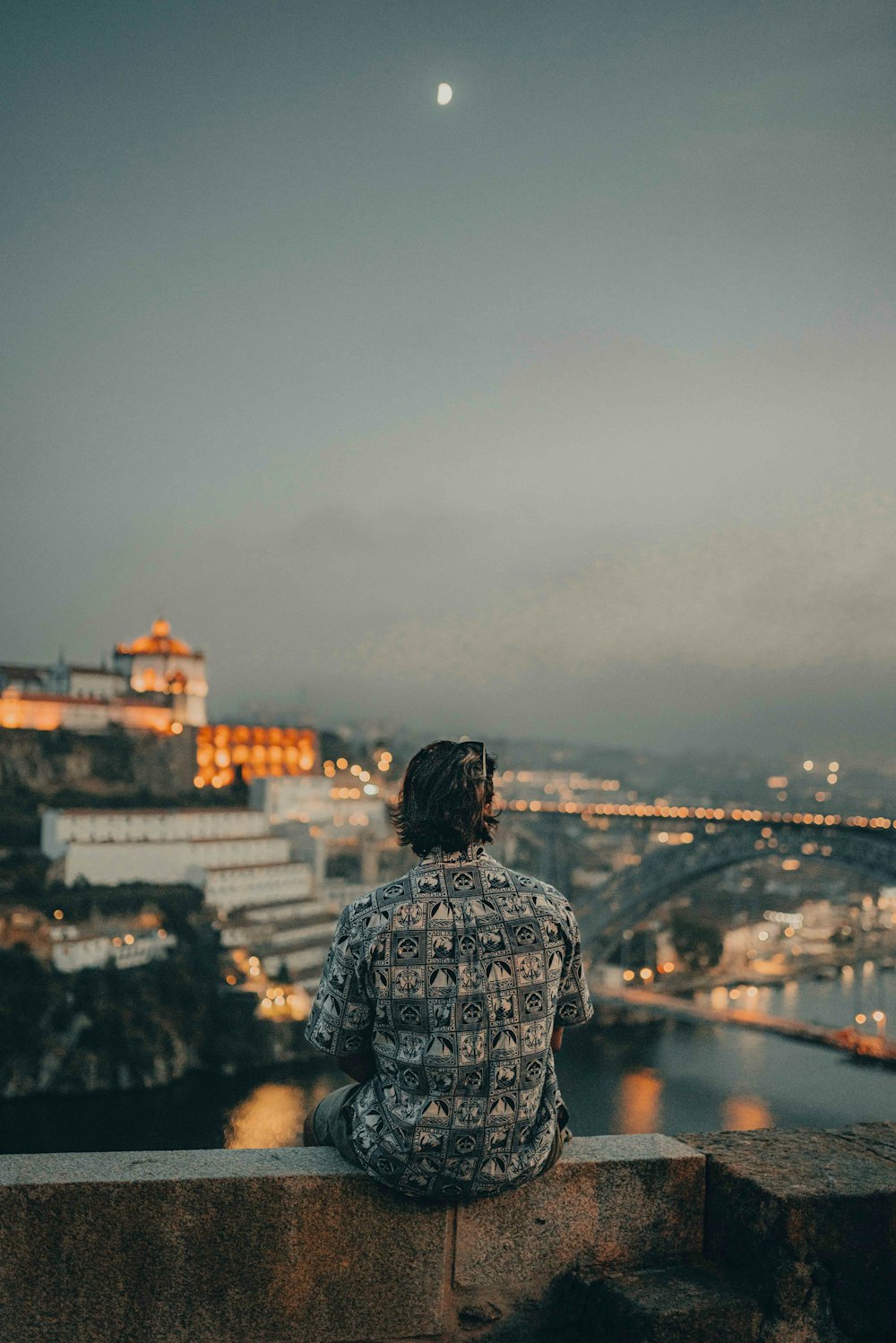 a person sitting on a ledge looking at a city