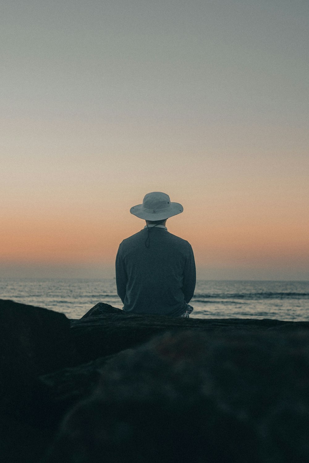 a man sitting on a rock looking out at the ocean