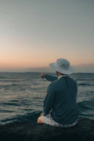 Golden hour shot of a person sitting by the beach wearing a classic brimora bucket hat.