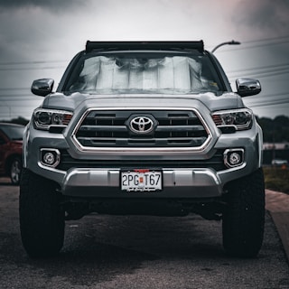 Mobile technician carefully installing a new windshield on a silver truck in a sunny driveway.