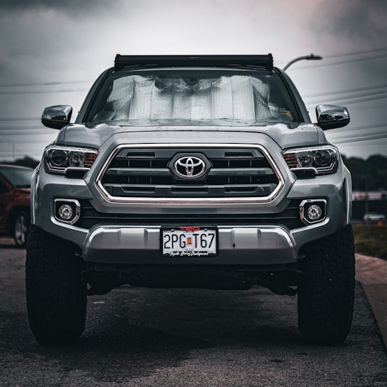 Mobile technician carefully installing a new windshield on a silver truck in a sunny driveway.
